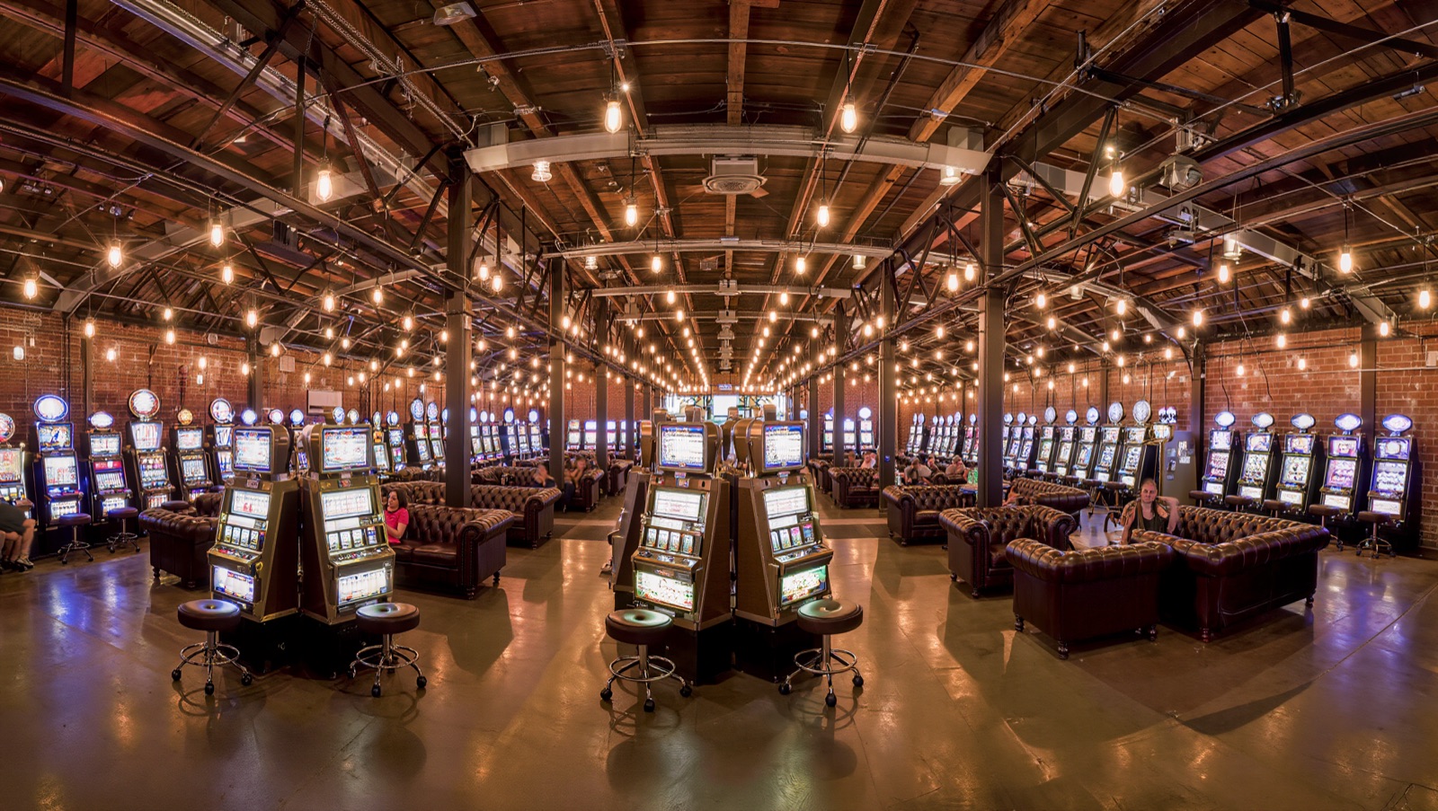 Concept render — the pusher hall: couches right beside clustered machines, warm bulb light down the timber hall